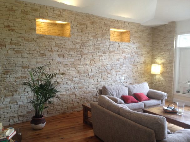 Sala de estar con pared de piedra, sofá gris y planta decorativa.
