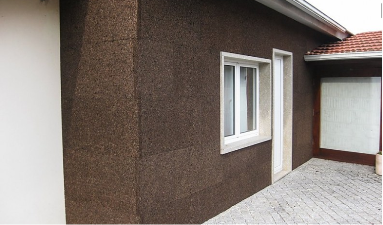 Fachada de casa con revestimiento marrón y ventanas blancas. Suelo de baldosas.