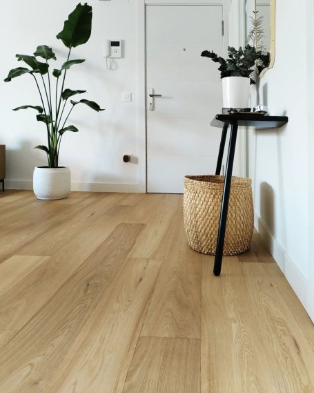Suelo de madera clara con una planta, una mesa negra y una cesta de mimbre en la esquina.
